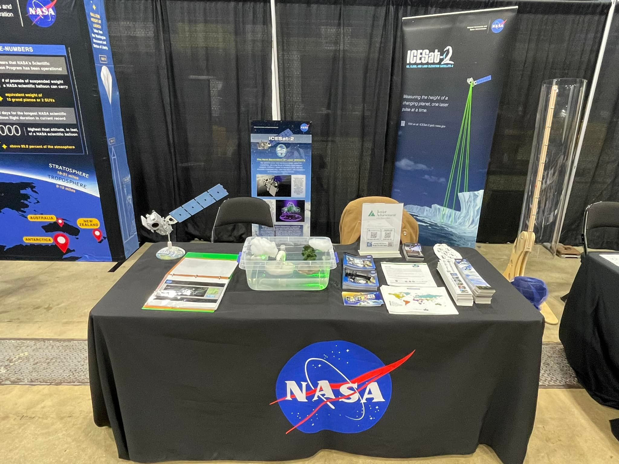 Image of a table with ICESat-2 materials in front of NASA and ICESat-2 signage